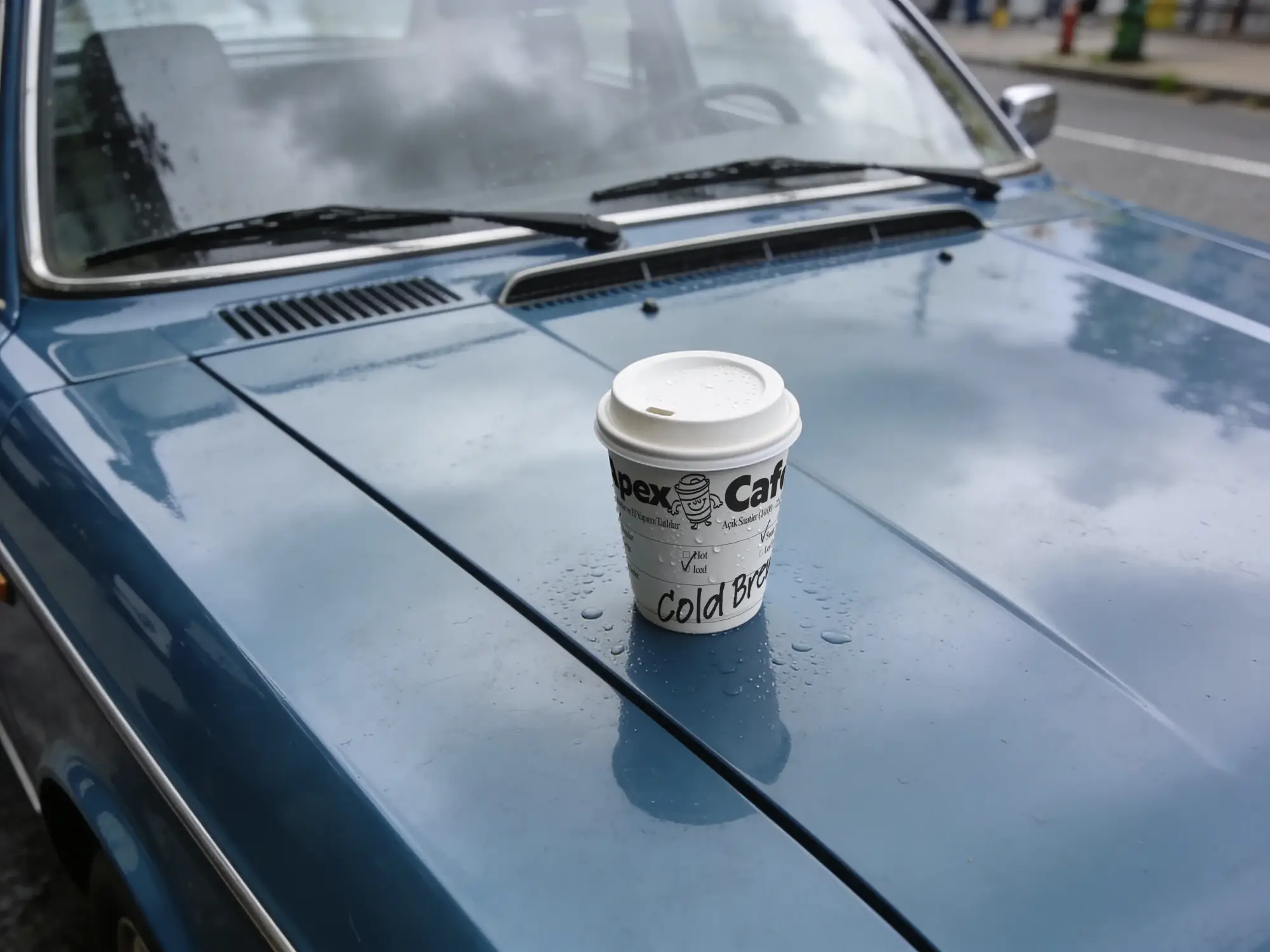 Coffee cup reading Apex Cafe on the bonnet of a wet blue car